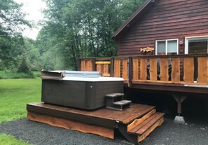 A hot tub on a wooden deck in front of a wooden cabin with a deck and a window.