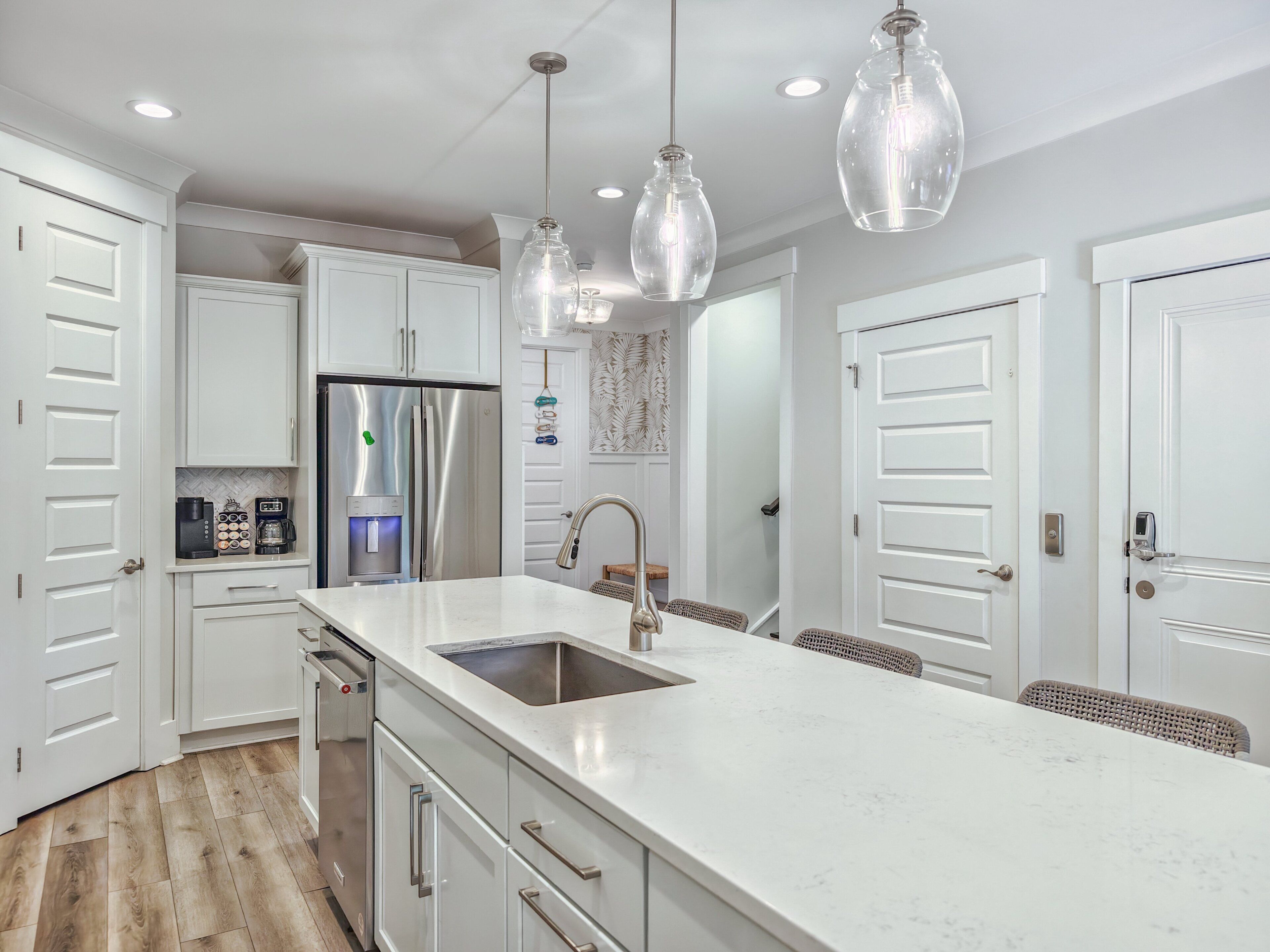 Una cucina moderna con mobili bianchi, elettrodomestici in acciaio inossidabile e illuminazione a sospensione.