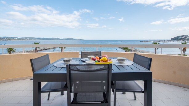 Una mesa con sillas en un balcón con vista a una playa y al mar.