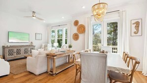 A modern living room with a dining area, wooden flooring, and large windows.
