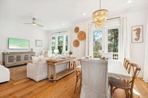 A modern living room with a dining area, wooden flooring, and large windows.