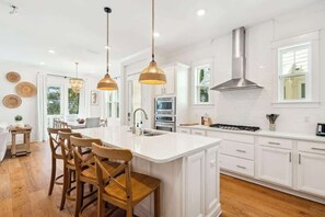 A modern kitchen with white cabinetry, a central island with bar stools, pendant lighting, and a stainless steel range hood.