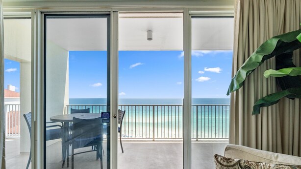 A balcony with a view of the ocean, a table with chairs, and a couch.