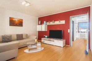 Un salon moderne avec un canapé, une table basse, un téléviseur à écran plat et un mur d’accent rouge.