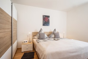 Une chambre à coucher avec un lit, des tables de chevet, une commode, une radio, une lampe, un tapis noir et un tableau accroché au mur.