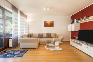 Un salon moderne avec un canapé, une table basse en verre, un téléviseur à écran plat et un mur d’accent rouge.