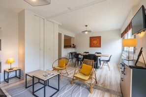 A room with a dining table, chairs, a TV, and a lamp.