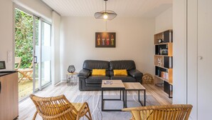 Ein modernes Wohnzimmer mit einer Couch, zwei Sesseln, einem Couchtisch, einem Bücherregal und einem Deckenventilator.
