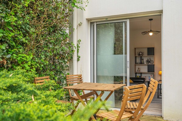 A patio with wooden furniture, a glass door leading to an interior space, and a wall covered with greenery.