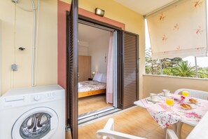 A balcony with a washing machine, a bed, and a breakfast table with orange juice.