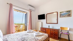 A bedroom with a bed, a wooden dresser, a chair, a TV, and a balcony with a view. - Apartment 'Lotus 4' with Shared Terrace, Wi-Fi and Air Conditioning (Corfu)