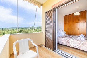 A balcony with a white chair, a bed with a floral bedspread, and a view of greenery.
