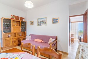 A room with a wooden cabinet, a purple sofa, a wooden dining table, and a bed.