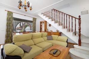 Ein Wohnzimmer mit Ecksofa, Couchtisch aus Holz, einer Treppe mit Holzspindeln und einer Chandelier.