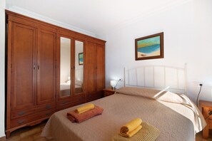 Ein Schlafzimmer mit einem großen Holzschrank, einem Bett mit beige farbenem Bettbezug und einem Gemälde an der Wand.