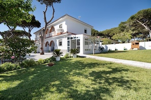 Un bâtiment blanc à deux étages, doté d’un balcon, entouré d’une pelouse bien entretenue et d’arbres.