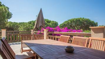 A wooden deck with a table and chairs, surrounded by a wooden railing and vibrant pink flowers.