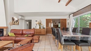 Een ruime woonkamer met een leren bank, eettafel en stoelen, een open haard en uitzicht door een groot raam.