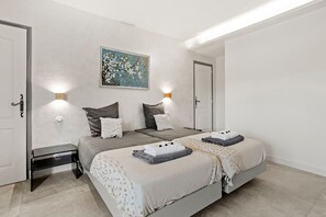 A bedroom with two beds, a nightstand, a wall-mounted light, and a painting.