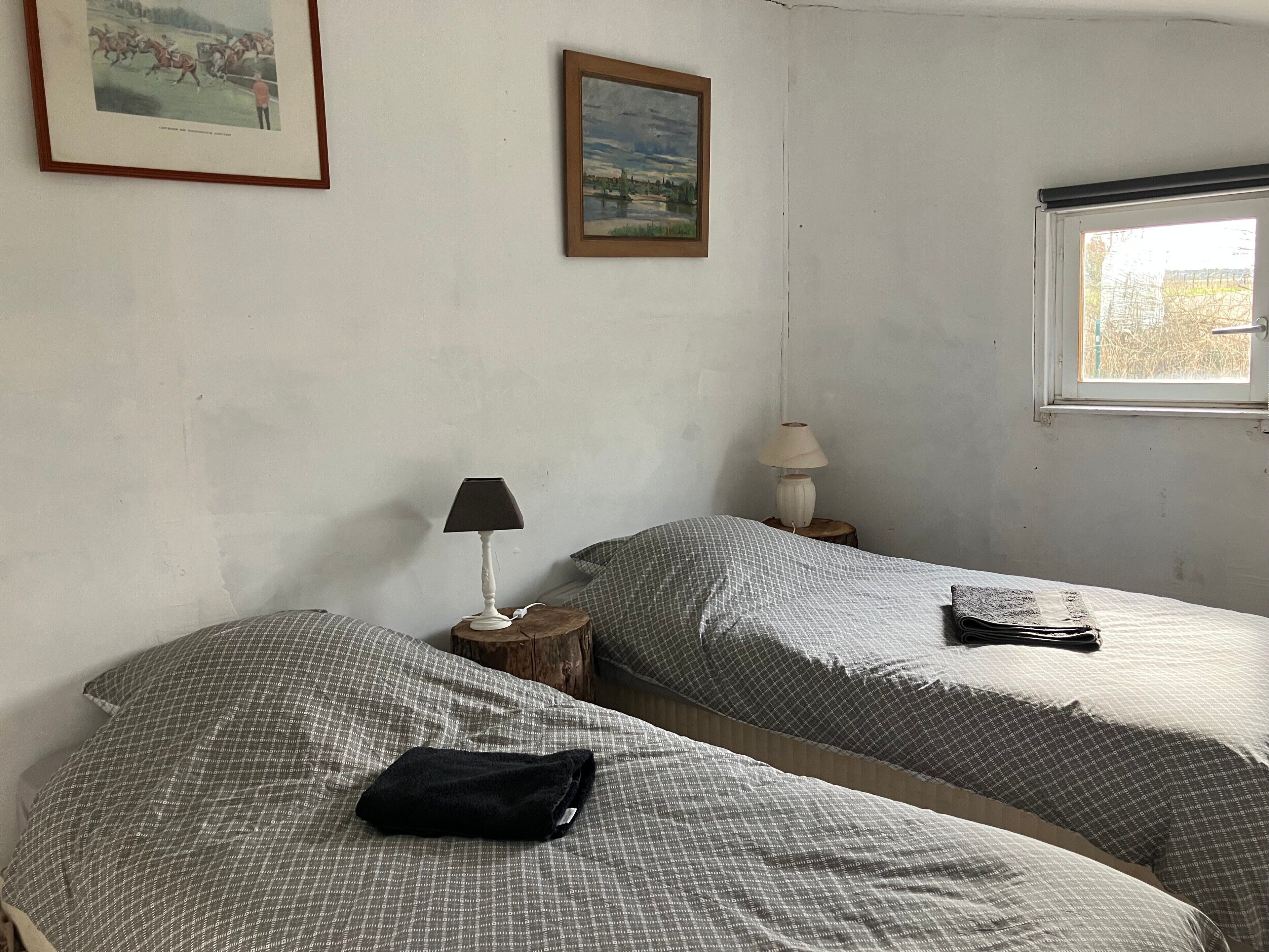 Una stanza con due letti, una finestra, una lampada e un quadro appeso al muro.