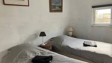 Una stanza con due letti, una finestra, una lampada e un quadro appeso al muro.