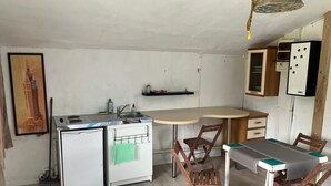 Une cuisine compacte équipée d’un évier, d’une cuisinière et d’un petit réfrigérateur. On y trouve une table à manger avec des chaises et un luminaire suspendu.