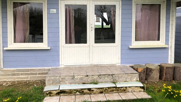 Une maison à l’extérieur bleu, avec une porte blanche dotée de panneaux de verre et un escalier en pierre menant à l’entrée.