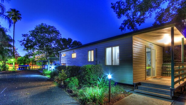 A single-story house with a porch and a covered entryway, surrounded by greenery and a wooden fence. - Highway Tourist Village (Narrabri)