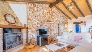 A stone wall, a fireplace, a television, and a white sofa in a living room. - Country House 'Ses Oliveres' with Mountain View, Wi-Fi and Air Conditioning (Campos)