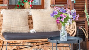 A wicker sofa with checkered cushions, a small round table with a vase of flowers, and a wicker chair. - Country House 'Ses Oliveres' with Mountain View, Wi-Fi and Air Conditioning (Campos)