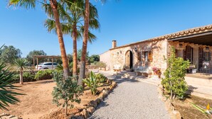 A stone building with a gravel path, palm trees, and a parked car. - Country House 'Ses Oliveres' with Mountain View, Wi-Fi and Air Conditioning (Campos)