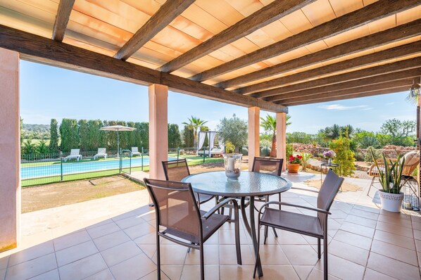 Um pátio coberto com piscina, cadeiras e uma mesa com um vaso.