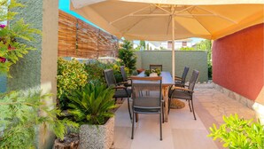 Une terrasse extérieure avec une table et des chaises, entourée de plantes et d’une clôture en bois.
