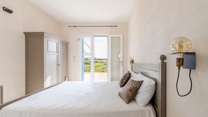 Een slaapkamer met een bed, een kledingkast, een nachtkastje met lamp en uitzicht door een deur.