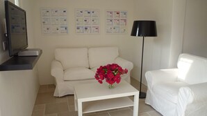 Ett vardagsrum med en vit soffa, ett soffbord med blommor, en tv och en lampa.