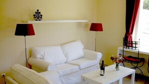 Um sofá branco, uma mesa de centro branca, um abajur vermelho e um vaso com flores.