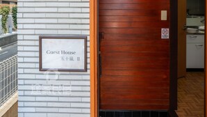 A hotel entrance with a brick wall, a wooden door, and a sign indicating it's a guest house.
