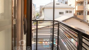 A narrow balcony with a metal railing, a glass door, and a view of a street with buildings.