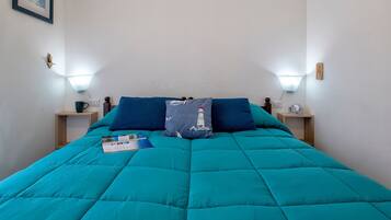 Un letto con biancheria color petrolio, due comodini con lampade, una sveglia e un quadro appeso alla parete.