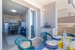Un ambiente compatto con angolo cottura, zona pranzo e un balcone con tavolo apparecchiato.
