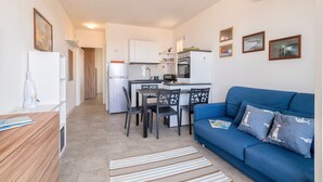 A compact living space with a kitchenette, a dining area, and a blue sofa with patterned cushions. - 'Ad Occhi Aperti - Castelsardo' Apartment with Sea View, Wi-Fi, and Air Conditioning (Castelsardo)