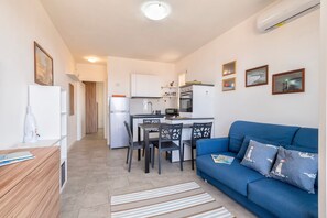 Un ambiente compatto con angolo cottura, zona pranzo e divano blu con cuscini decorati.