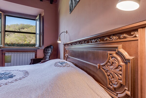 A bedroom with a large window, a bed with a decorative headboard, a bedside lamp, and a view of the outdoors.