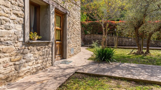 A stone building with a wooden door and window, a paved pathway, and a small garden with plants and trees. - Farmhouse 'Agriturismo Il Ponte - Frantoio' with Mountain View, Private Garden and Wi-Fi (Vicchio)