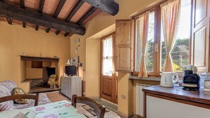 A cozy room with a fireplace, wooden ceiling beams, a dining table with floral tablecloth, and a kitchen area with a kettle and coffee maker. - Farmhouse 'Agriturismo Il Ponte - Frantoio' with Mountain View, Private Garden and Wi-Fi (Vicchio)