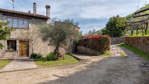 A stone house with a paved driveway, a wooden door, and a small garden with a tree and potted plants. - Farmhouse 'Agriturismo Il Ponte - Frantoio' with Mountain View, Private Garden and Wi-Fi (Vicchio)