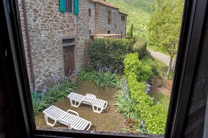 Un edificio de piedra con jardín, dos sillones blancos y vistas a un paisaje verde.