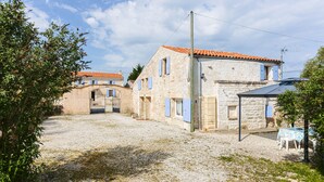 A stone building with a gravel courtyard, a small table with chairs, and a blue door. - Holiday Home 'La Rétaise' with Private Terrace and Garden (Romegoux)