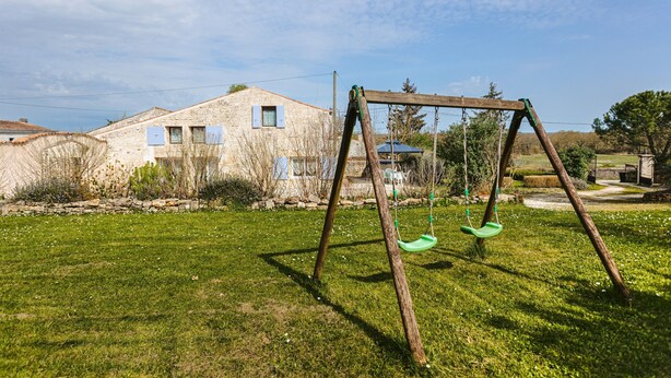 A wooden swing set in a grassy yard with a stone building in the background. - Holiday Home 'La Rétaise' with Private Terrace and Garden (Romegoux)