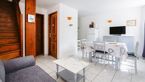 A living area with a sofa, a dining table with chairs, a TV, and a kitchen area with a refrigerator. - Holiday Home 'La Rétaise' with Private Terrace and Garden (Romegoux)